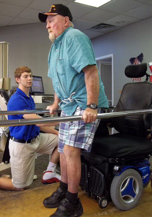 Man Getting Up from Wheelchair and Walking in Parallel Bars with Staff