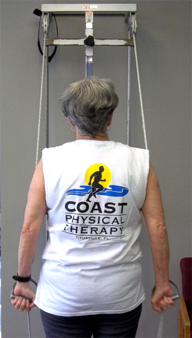 Woman Using Pulleys, Arms straight at Side while pulling handles.
